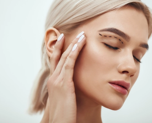 Plastische Chirurgie. Eine schöne junge blonde Frau mit geschlossenen Augen, die ihr Gesicht berührt, auf dem eine Skizze zu sehen ist.