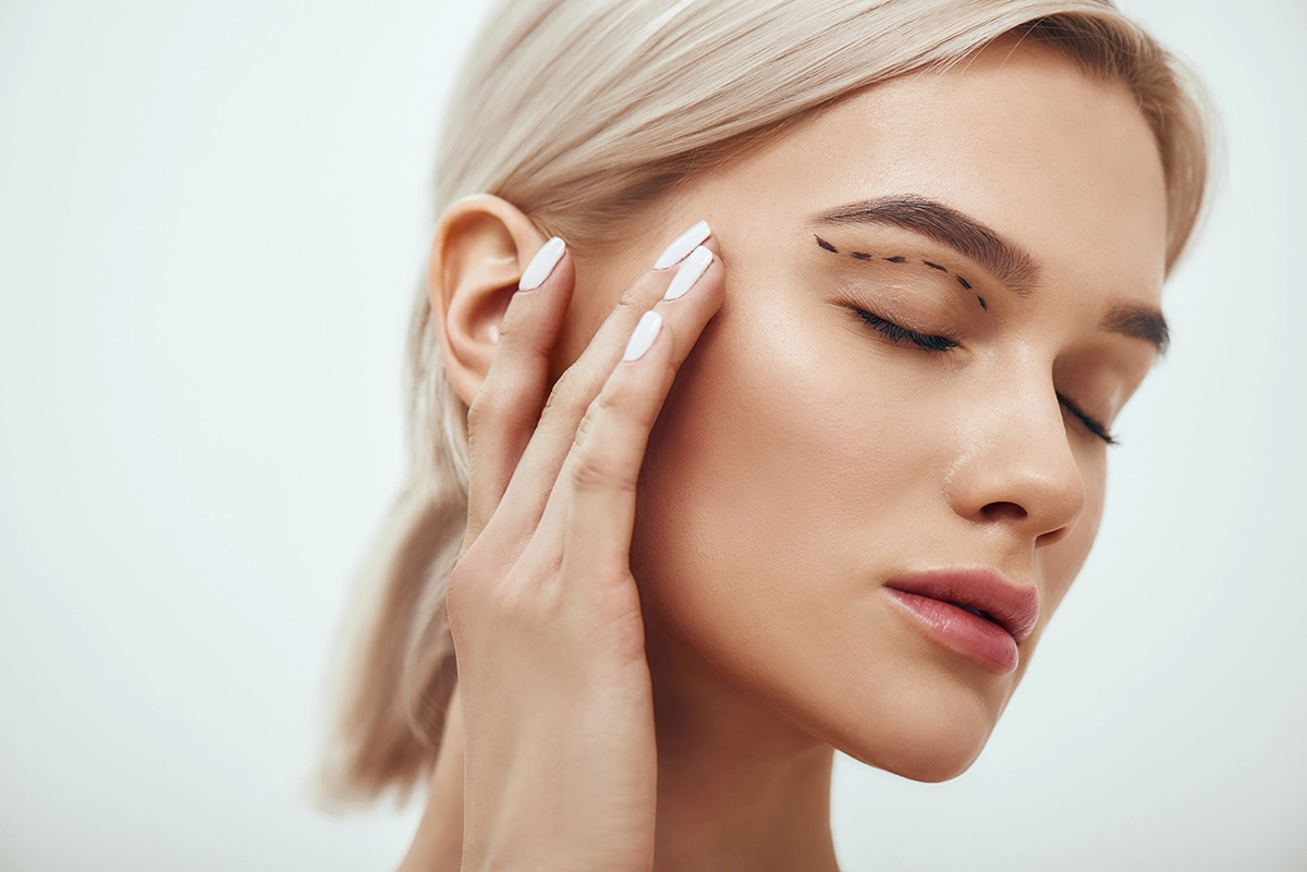 Plastische Chirurgie. Eine schöne junge blonde Frau mit geschlossenen Augen, die ihr Gesicht berührt, auf dem eine Skizze zu sehen ist.